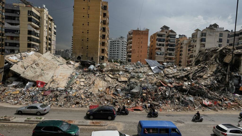 ARCHIV - Anwohner fahren an den Trümmern zerstörter Gebäude in Dahija, einem südlichen Vorort von Beirut, Libanon, vorbei. Foto: Bilal Hussein/AP/dpa