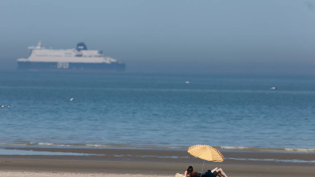 Menschen unter einem Sonnenschirm am Strand von Gravelines. Foto: Jean-Francois Badias/AP/dpa/Archivbild