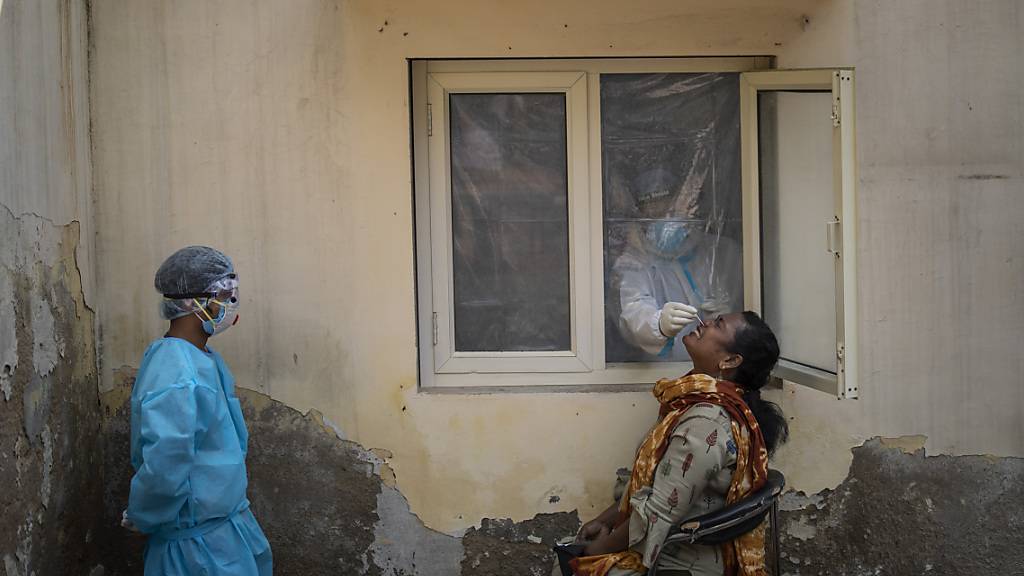 dpatopbilder - Ein mit einem Schutzanzug bekleideter Mitarbeiter des Gesundheitswesens nimmt bei einer Frau in einem Covid-19-Testzentrum im indischen Neu Delhi eine Nasenabstrichprobe. Foto: Altaf Qadri/AP/dpa