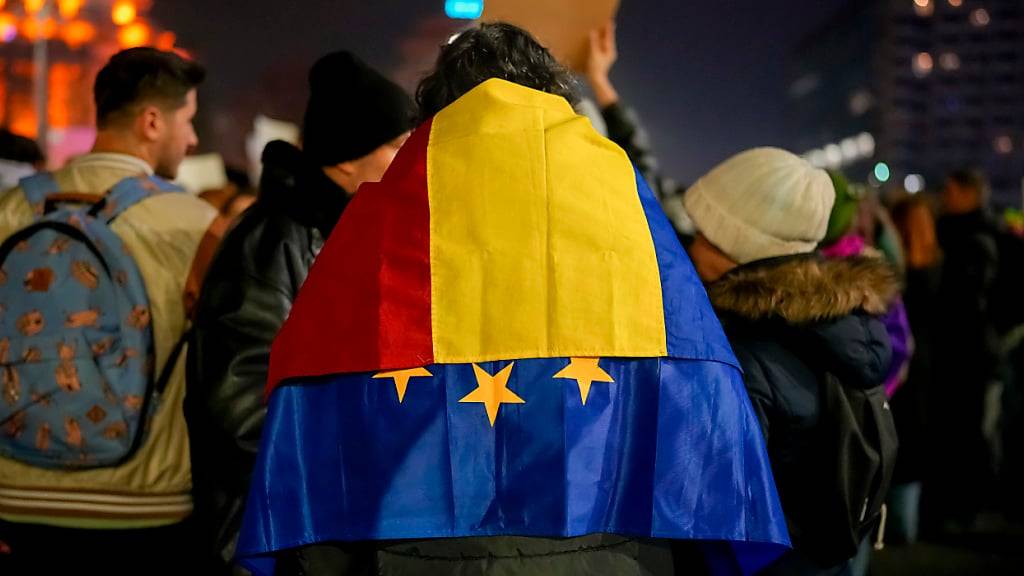 Ein Mann mit der rumänischen und der EU-Fahne über den Schultern nimmt an einem Protest gegen Georgescu, den unabhängigen Kandidaten für das rumänische Präsidentenamt, der die erste Wahlrunde gewonnen hat, teil. Foto: Vadim Ghirda/AP/dpa
