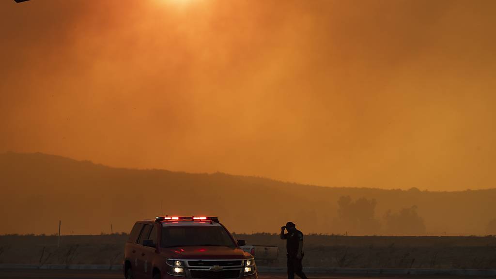 Ein Polizeiauto steht im dichten Rauch eines Waldbrandes. Ein schnell um sich greifendes Feuer hat Einwohner im US-Staat Kalifornien etwa 70 Kilometer südöstlich von Los Angeles aufgeschreckt. Foto: Mindy Schauer/The Orange County Register/AP/dpa