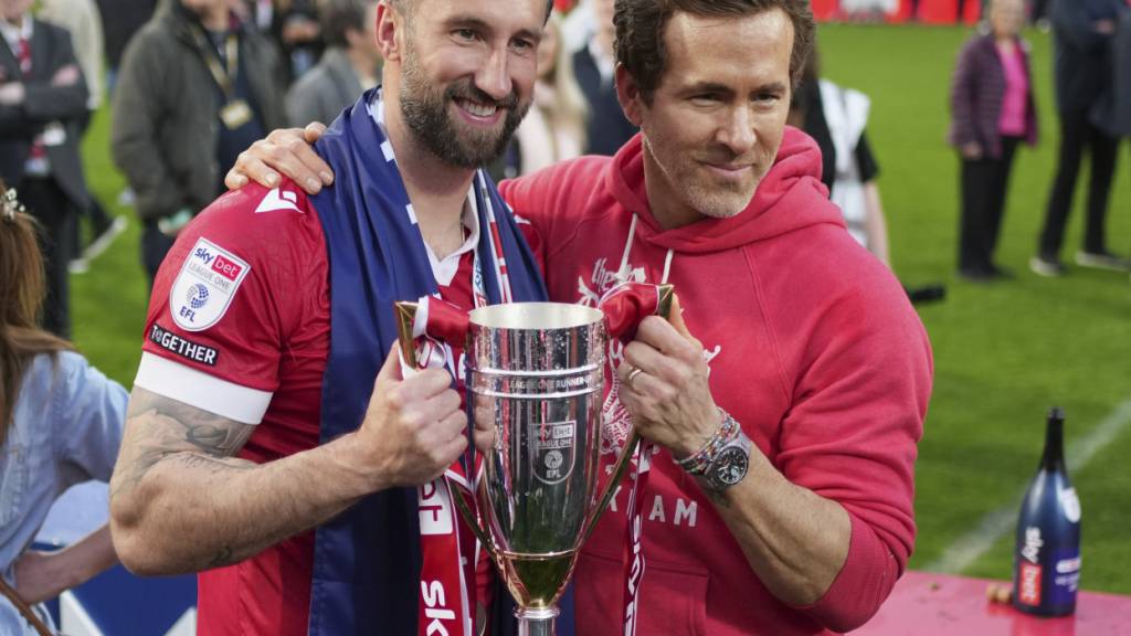 Der Hollywood-Star Ryan Reynolds, der seit gut fünf Jahren Co-Besitzer des AFC Wrexham ist, und Spieler Ollie Palmer (links) posieren nach dem Aufstieg in die Championship in der vergangenen Saison mit dem Pokal