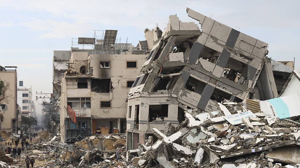 Palästinenser gehen an einem Gebäude vorbei, das bei einer israelischen Bombardierung des Gazastreifens zerstört wurde. Foto: Mohammed Hajjar/AP/dpa