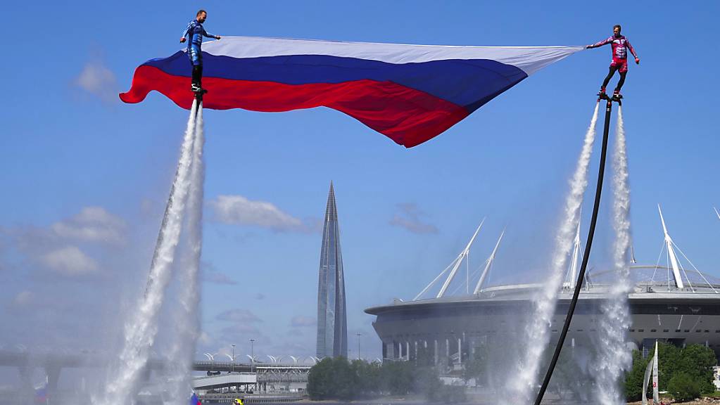 Mitglieder der russischen Wasserflugstaffel tragen bei einer Vorführung zum Nationalfeiertag die russische Nationalflagge über einen Kanal. Foto: Dmitri Lovetsky/AP/dpa