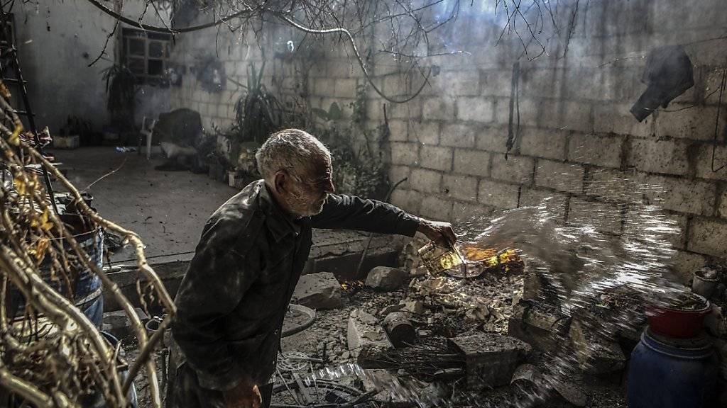 Ein Mann versucht nach Luftangriffen ein Feuer hinter seinem Haus in einem Vorort von Damaskus zu löschen. Mit Inkrafttreten der Waffenruhe soll ab Montagabend vorerst Schluss sein mit Luftangriffen.