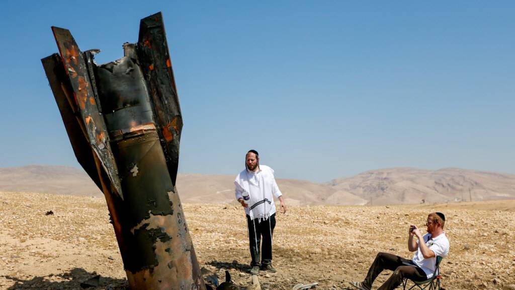 Israelische ultraorthodoxe jüdische Männer inspizieren das Wrack einer Rakete, die nach einem iranischen Angriff nahe der Stadt Jericho im Westjordanland aus dem Boden ragt. Foto: Jamal Awad/dpa