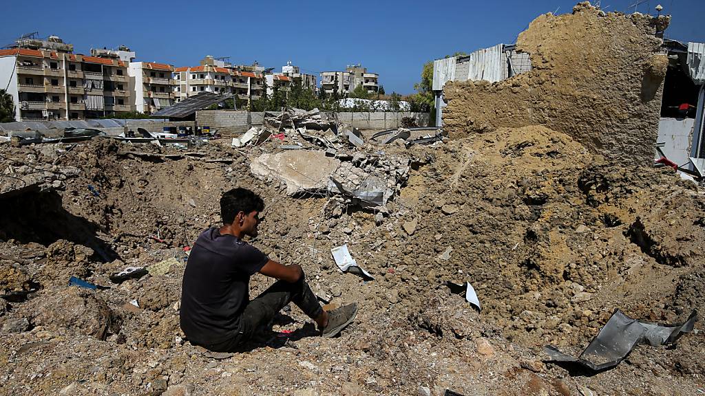 Ein Libanese sitzt am Rande eines Kraters, der durch einen nächtlichen israelischen Luftangriff in der Gegend von Jiyeh an der Küstenstraße zwischen der südlichen Hafenstadt Sidon und Beirut entstanden ist. Foto: Marwan Naamani/dpa