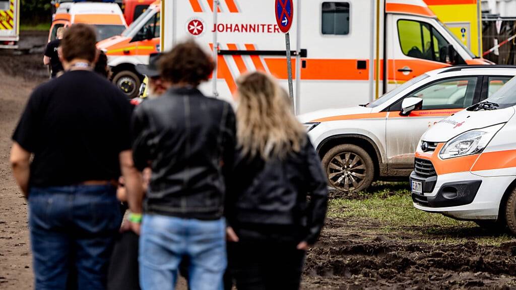Festivalbesucher stehen vor dem im Schlamm stehenden Fuhrpark an Rettungsfahrzeugen. Foto: Axel Heimken/dpa