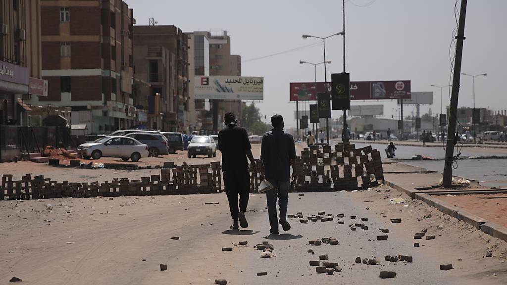 Zwei Personen gehen auf einer Straße auf der Steine liegen und eine behelfsmäßigen Barrikade aufgebaut ist. Foto: Marwan Ali/AP/dpa