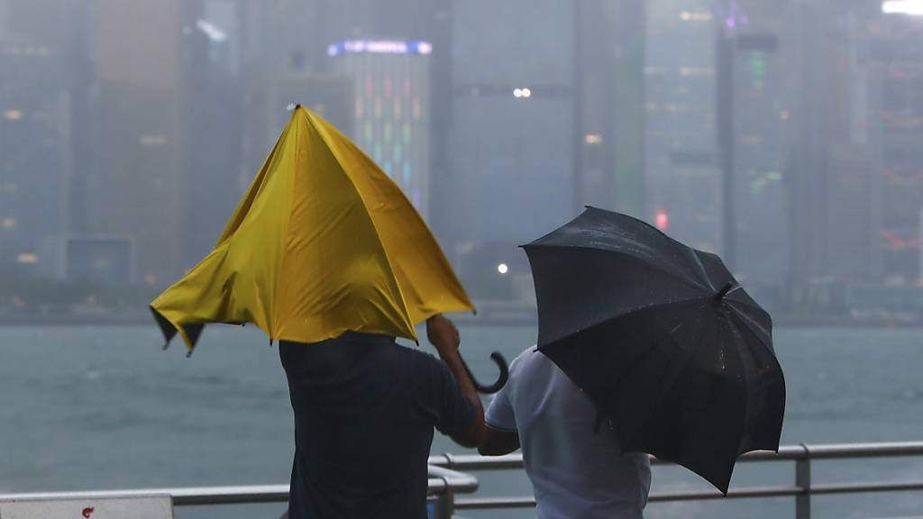 Menschen mit Regenschirmen kämpfen gegen starken Wind und Regen des Taifuns «Saola» an. Begleitet von starken Regenfällen und Windböen hat der Taifun «Saola» die Küstengewässer Südchinas und Hongkongs erreicht. Foto: Daniel Ceng/AP/dpa
