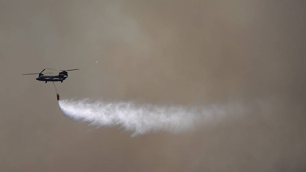 Ein Militärhubschrauber wirft Wasser auf ein Feuer auf ein Brandgebiet. Foto: Thanassis Stavrakis/AP/dpa