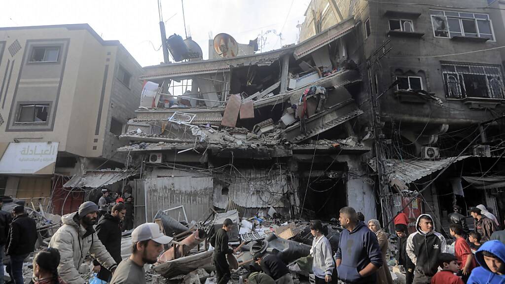 dpatopbilder - Palästinenser gehen vor den stark beschädigten Gebäuden nach einem israelischen Angriff. Foto: Mohammed Talatene/dpa