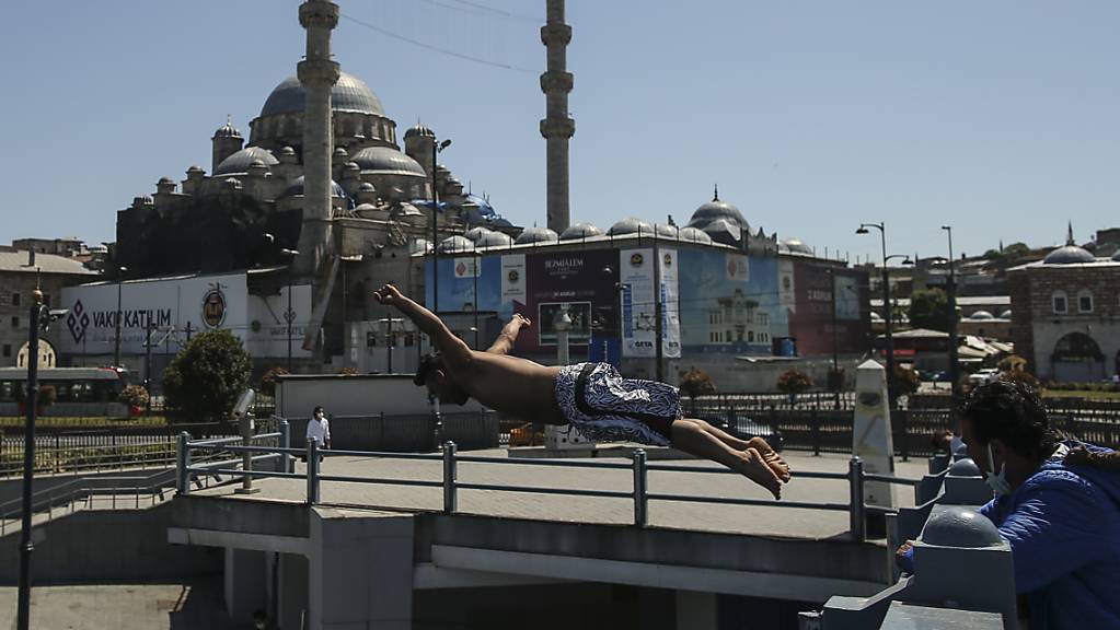 Vor dem Hintergrund der historischen Neuen Moschee springt ein Jugendlicher von der Galata Brücke in den Bosporus.