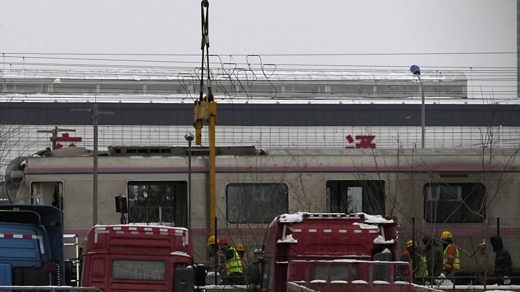 Arbeiter befestigen einen Kran an Zugwaggons an der Stelle, wo sich der Zug-Unfall in Peking ereignete. Foto: Ng Han Guan/AP/dpa