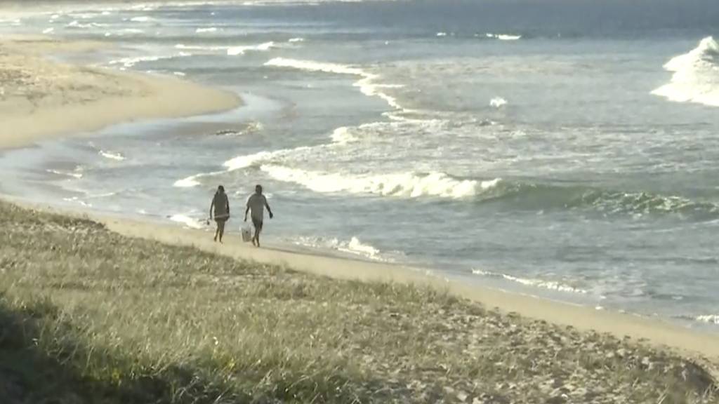 In diesem Standbild aus einem Video gehen Menschen an einem Strand in Tuncurry, Australien entlang. Foto: Uncredited/Australian Broadcasting Corporation via AP/dpa