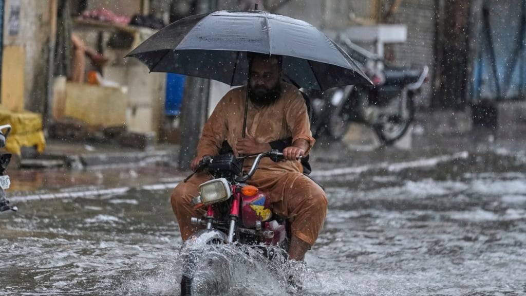 dpatopbilder - Ein Motorradfahrer fährt mit Regenschirm durch eine überschwemmte Straße in Rawalpindi. Foto: Anjum Naveed/AP/dpa