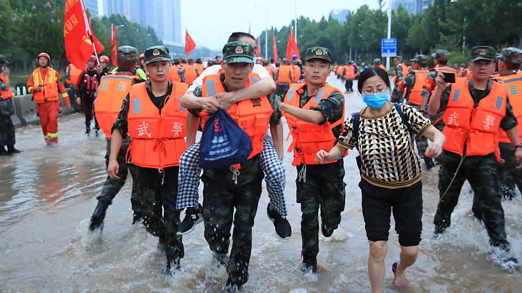 Mitarbeiter des Militärs tragen Patienten eines Krankenhauses über eine überschwemmte Straße. Laut Angaben des chinesische Staatsfernsehens am Freitag ist die Zahl der Toten nach den schweren Überschwemmungen in der chinesischen Metropole Zhengzhou auf 56 gestiegen. Foto: Uncredited/CHINATOPIX/AP/dpa