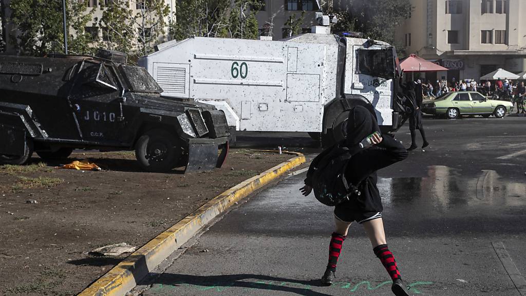 Eine Demonstrantin wirft eine Flasche auf einen Wasserwerfer der Polizei während einer Demonstration in Santiago de Chile am Internationalen Frauentag. Foto: Esteban Felix/AP/dpa