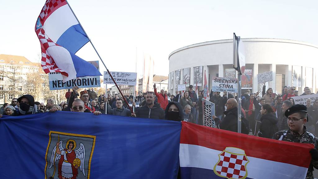 Menschen stehen während eines Protestes mit Fahnen und Plakaten auf der Straße. Am Samstag sind in der kroatischen Hauptstadt Zagreb Tausende Menschen durch die Straßen gezogen, um gegen die Corona-Maßnahmen der kroatischen Regierung zu protestieren. Foto: -/AP/dpa