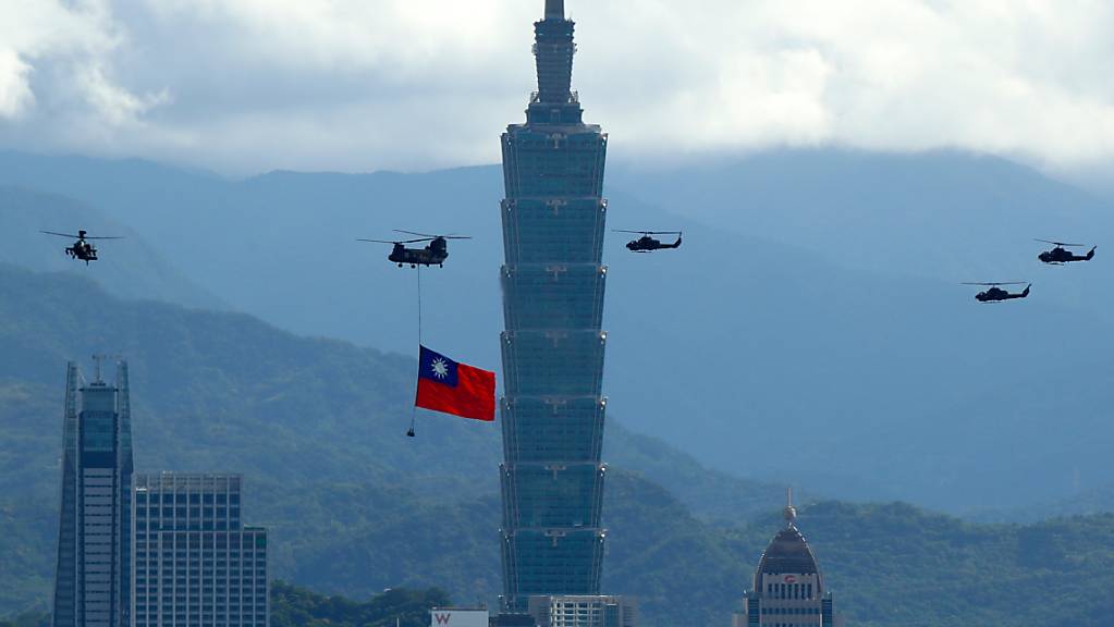 Ein Militärhubschrauber zieht eine riesige Taiwan-Fahne hinter sich her und fliegt vor den Feierlichkeiten des Nationalfeiertag am Hochhaus «Taipei 101» vorbei. Foto: Daniel Ceng Shou-Yi/ZUMA Press Wire/dpa
