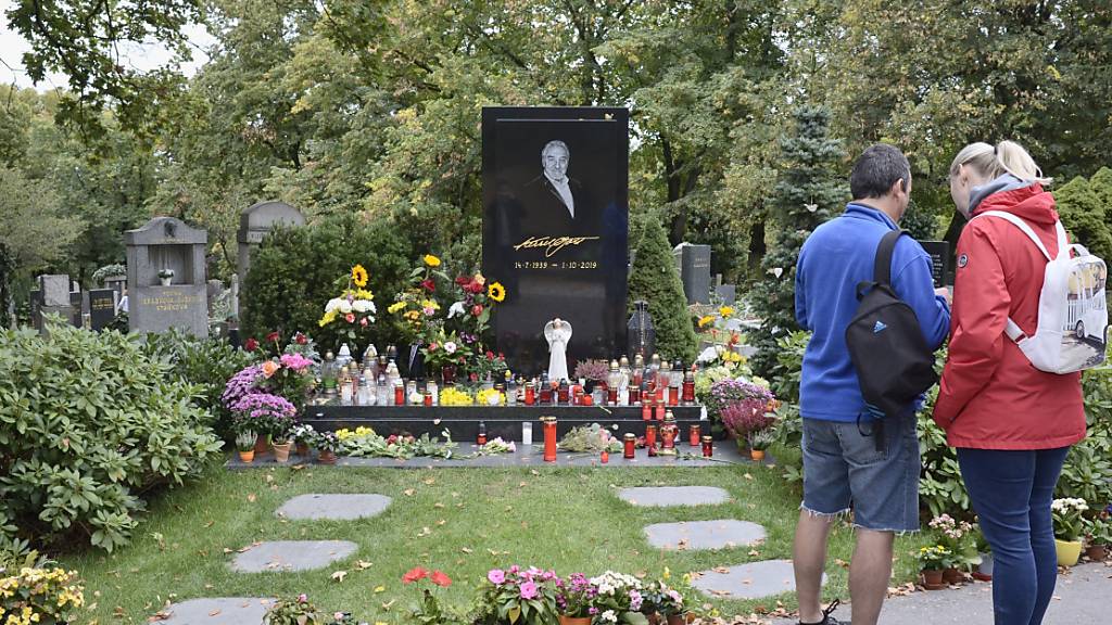 Menschen stehen am Grab des tschechischen Sängers Karel Gott auf dem Malvazinky-Friedhof, wo frische Blumen stehen und Kerzen brennen. Vor einem Jahr, am 1. Oktober 2019, war der Sänger im Alter von 80 Jahren gestorben. Foto: Michael Heitmann/dpa