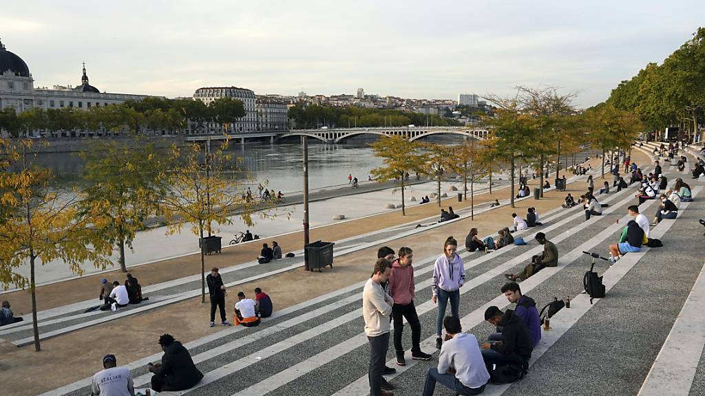 Menschen sitzen entlang des Flusses Rhone. Die französischen Behörden haben die Stadt Lyon auf die höchste Warnstufe gesetzt. Versammlungen sind untersagt und Bars werden schließen müssen. Foto: Laurent Cipriani/AP/dpa
