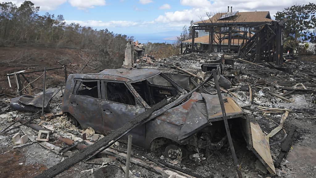 Die verkohlten Überreste eines Fahrzeugs stehen  in Kula, Hawaii, neben einem von einem Waldbrand zerstörten Haus. Foto: Rick Bowmer/AP