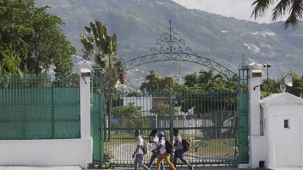 Fußgänger gehen am Tor des Präsidentenpalast vorbei. Präsident Moise war in der Nacht zum Mittwoch gegen 1.00 Uhr (Ortszeit) in seiner Residenz erschossen worden. Trotz erster Festnahmen ist die Lage in Haiti weiterhin angespannt. Foto: Joseph Odelyn/AP/dpa
