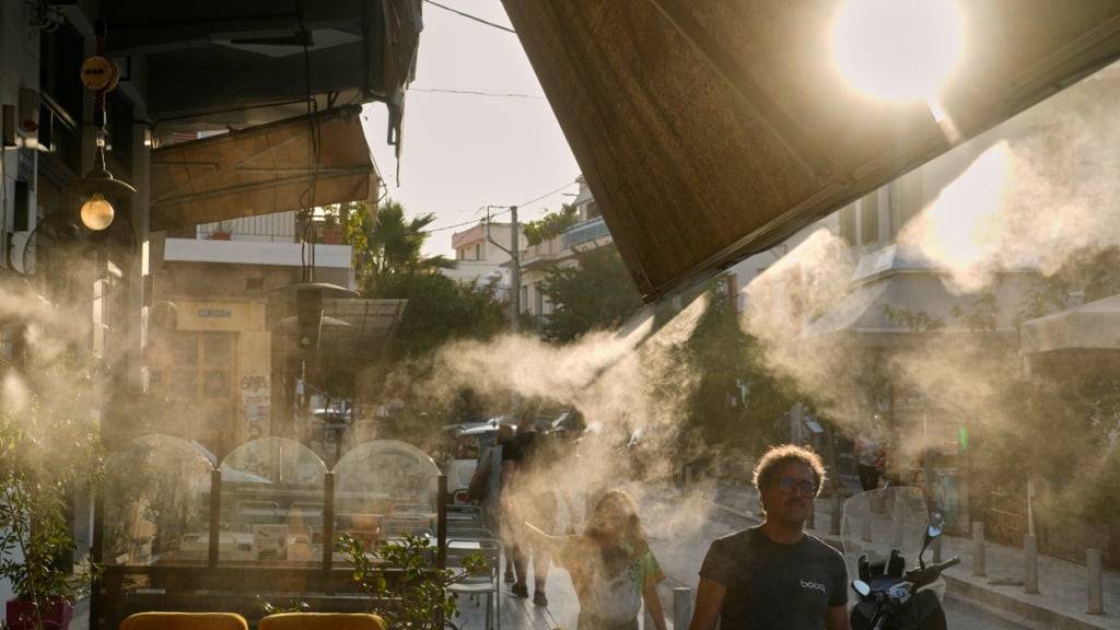 Fußgänger gehen während einer Hitzewelle neben einer Nebelmaschine im Athener Stadtteil Thisio spazieren. Foto: Petros Giannakouris/AP/dpa