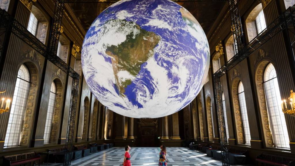Mitarbeiterinnen posieren mit Luke Jerrams Installation eines riesigen Globus namens «Gaia» im Royal Naval College in Greenwich (GB). (Archivbild)