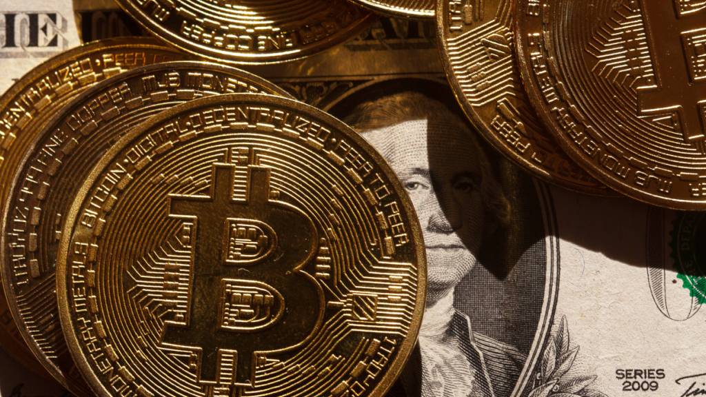 ILLUSTRATION - Goldene Bitcoin-Münzen liegen auf einer US-Dollar-Banknote. (zu dpa: «Krypto-Investor wegen Entführung und Folter angeklagt») Foto: Fernando Gutierrez-Juarez/dpa