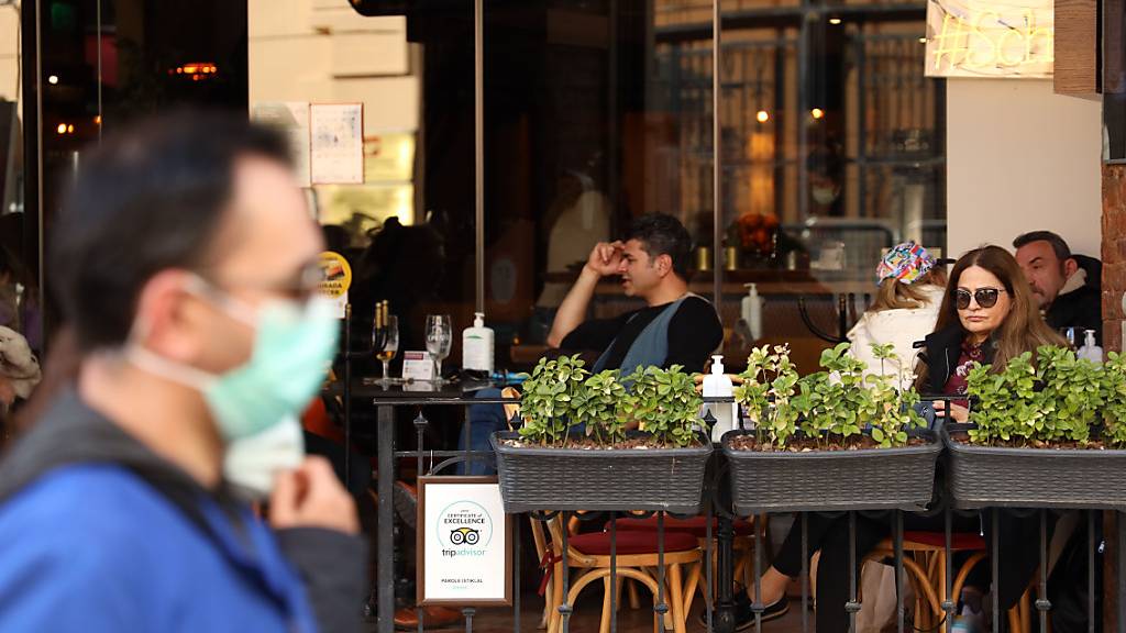 Ein Mann mit Mund-Nasen-Schutz läuft an einem Café in Istanbul vorbei, in dem einige Menschen sitzen. Foto: Shady Al-Assar/APA Images via ZUMA Wire/dpa