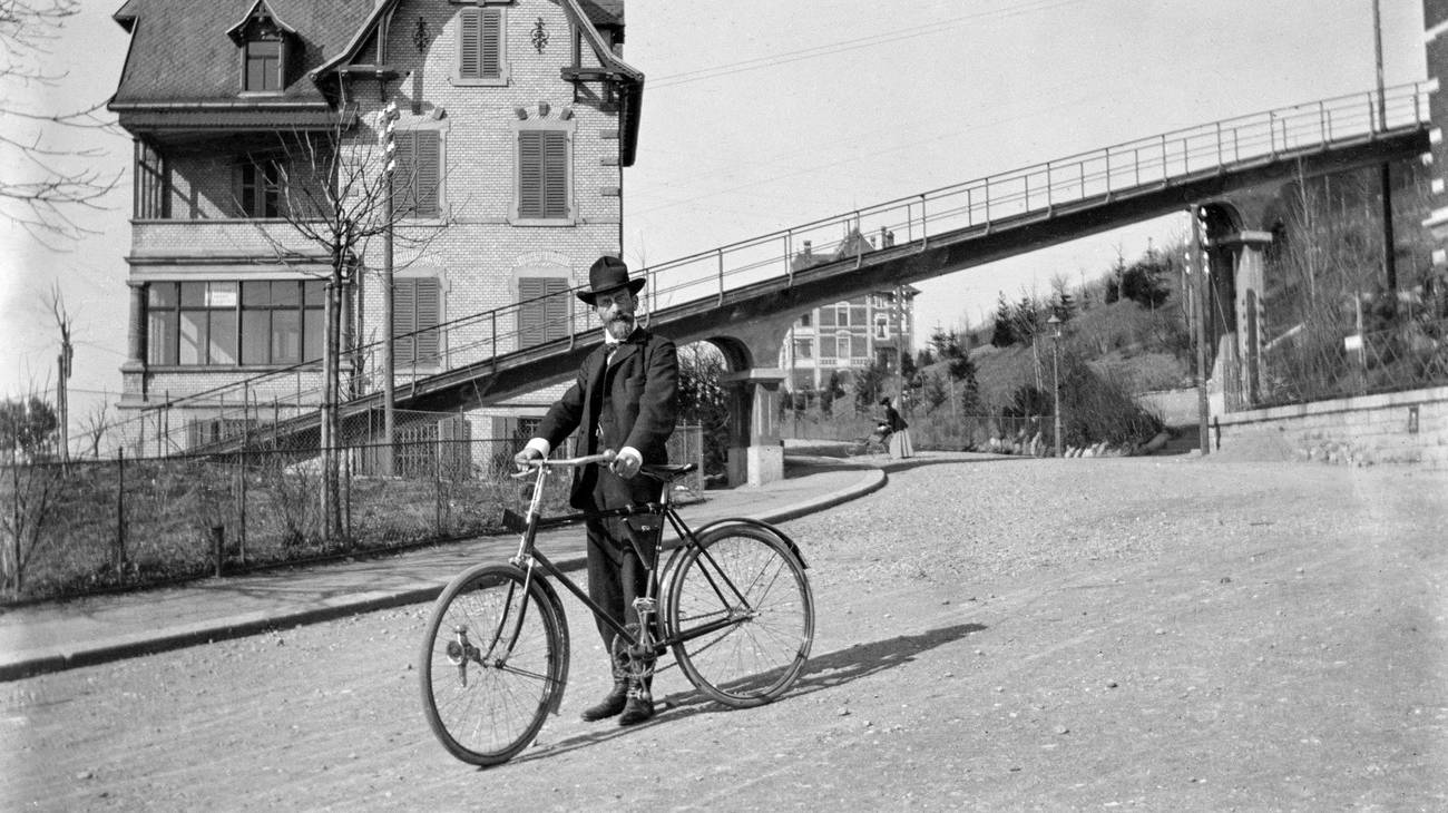 Ein Mann mit Fahrrad vor einer Bruecke der Seilbahn Rigiblick in Zuerich, aufgenommen um 1901