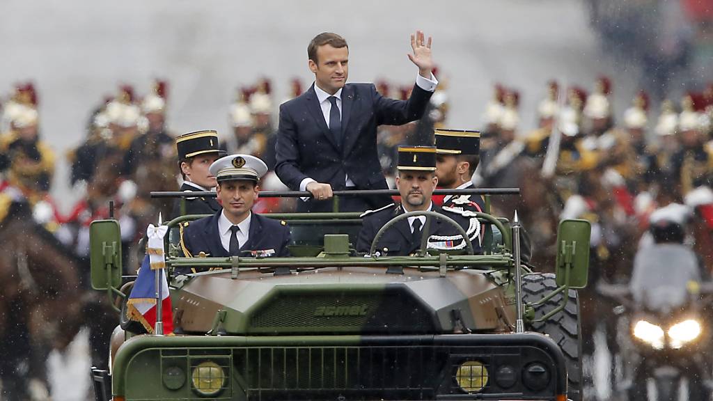 ARCHIV - Der französische Präsident Emmanuel Macron (M) wird in einem Militärfahrzeug bei einer Parade über die Champs-Elysees in Paris gefahren. Frankreich verzichtet wegen der Corona-Krise auf die traditionelle Militärparade am Nationalfeiertag 14. Juli. Foto: Michel Euler/Pool AP/dpa