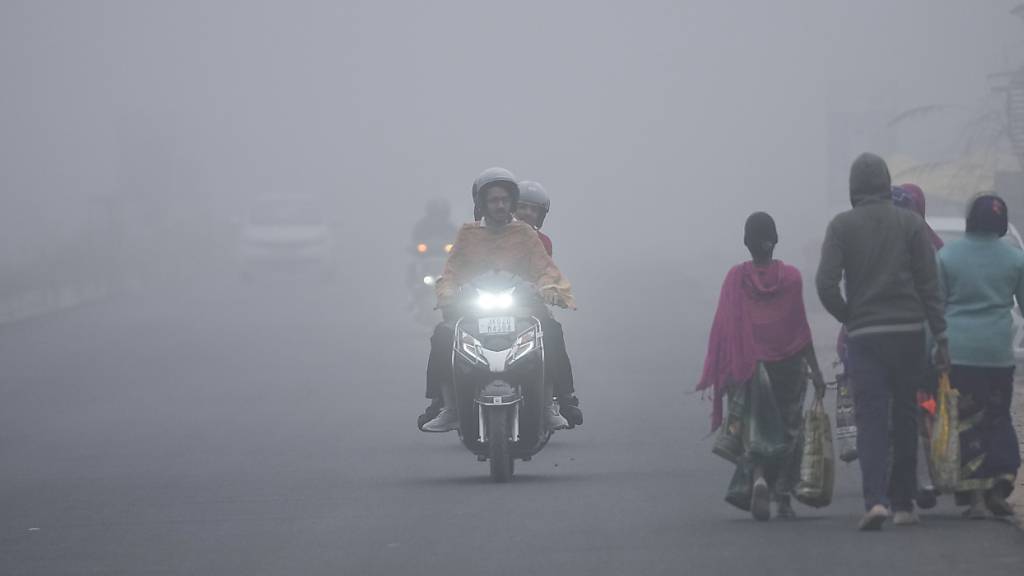 Pendler fahren an einem kalten Morgen durch dichten Nebel. Foto: Channi Anand/AP