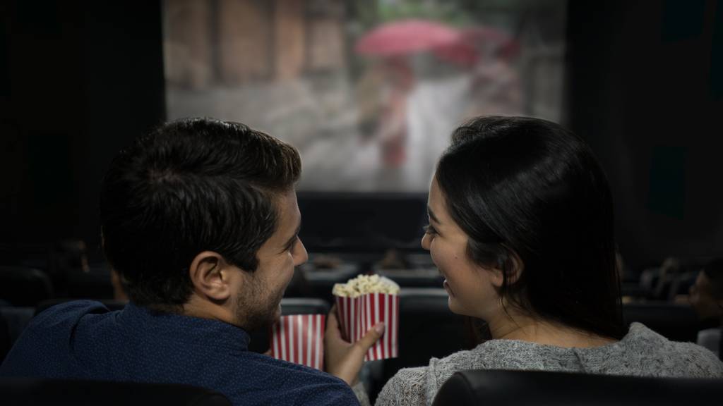 Happy Latin American couple lauging at the movies eating popcorn and having fun