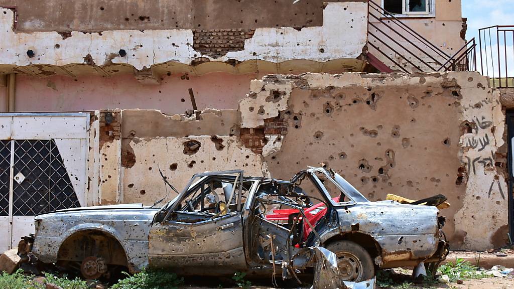 ARCHIV - Ein zerstörtes Auto in der sudanesichen Stadt Omdurman steht vor einem Haus voller Einschüsse. Foto: Mudathir Hameed/dpa