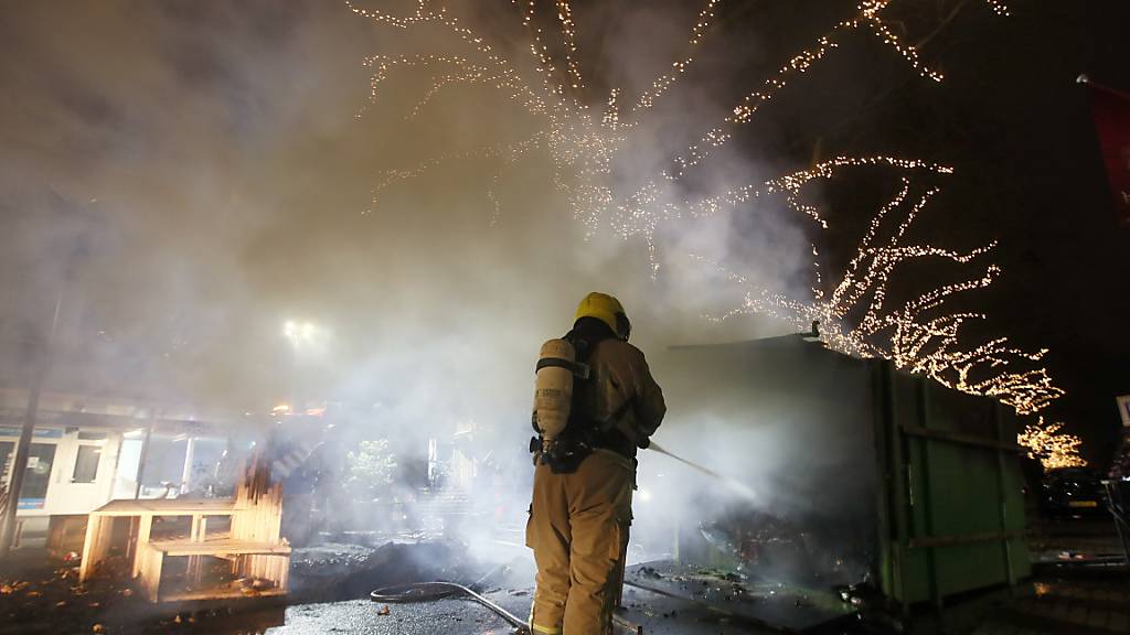 Krawalle in Rotterdam: Ein Feuerwehrmann löscht einen Container, der bei Protesten gegen eine landesweite Ausgangssperre in Brand gesetzt wurde. Foto: Peter Dejong/AP/dpa