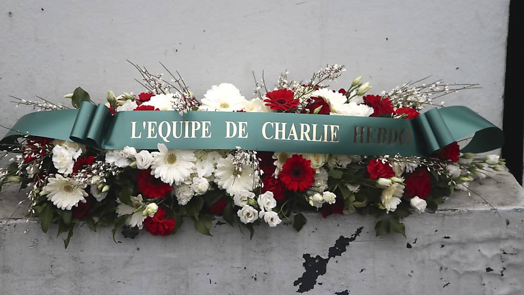 Ein Blumenkranz mit der Aufschrift «Das Team von Charlie Hebdo» liegt vor dem ehemaligen Bürogebäude des Satiremagazins. Foto: Michel Euler/POOL AP/AP/dpa