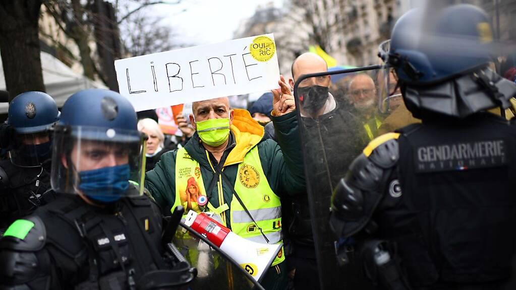 Ein Demonstrant in Paris hält vor Polizisten ein Schild mit der Aufschrift «Freiheit» in die Höhe. Foto: Christophe Archambault/AFP/dpa