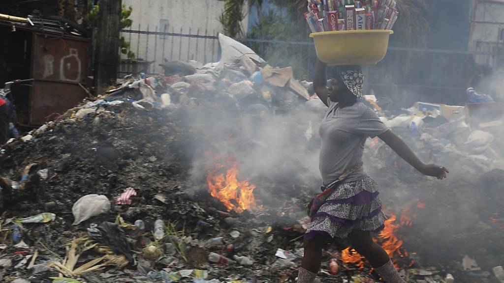 ARCHIV - Ein Straßenverkäufer geht in Port-au-Prince, Haiti, an einem Haufen brennender Abfälle vorbei. Foto: Odelyn Joseph/AP/dpa