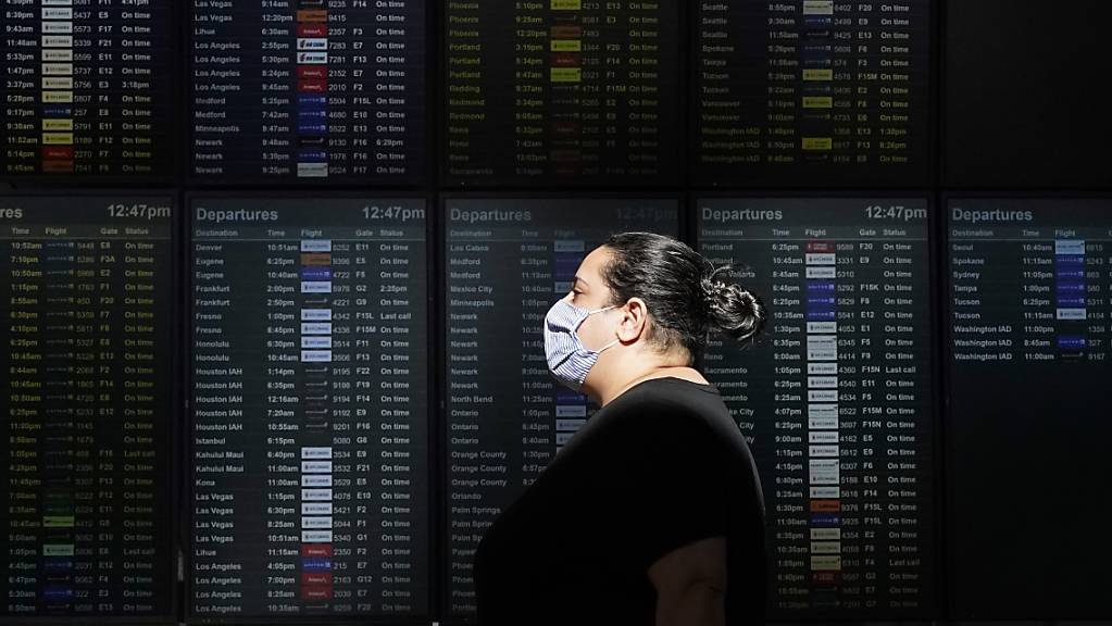ARCHIV - Eine Frau mit Mund-Nasen-Schutz geht an einer Anzeigetafel am Internationalen Flughafen von San Francisco vorbei. Foto: Jeff Chiu/AP/dpa