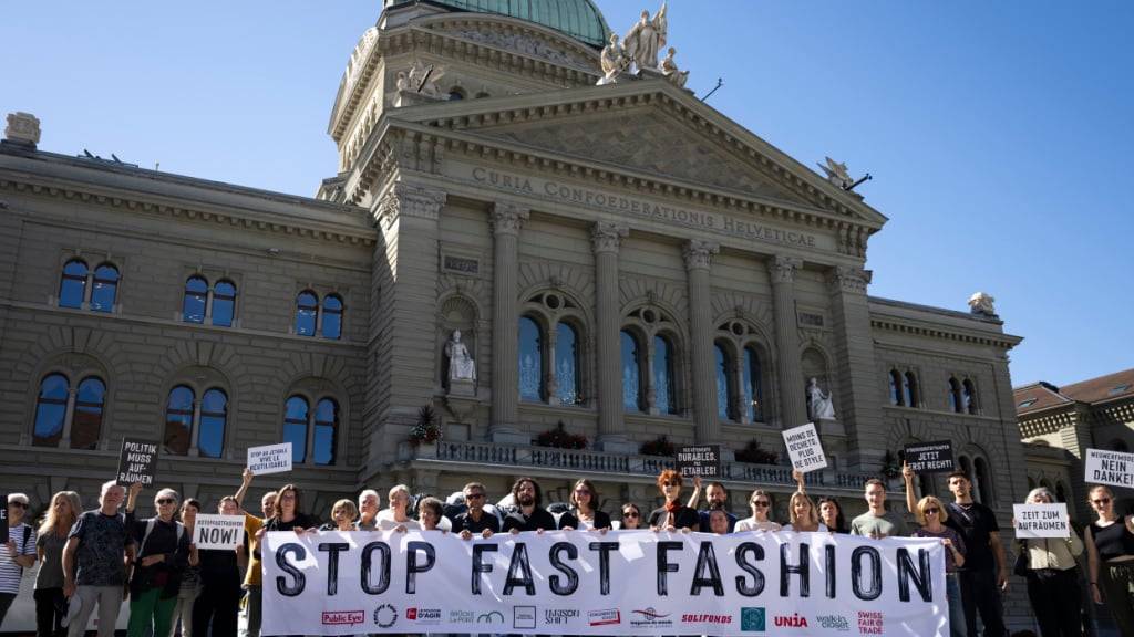 Freiwillige posieren am Mittwoch mit Plakaten und einem Transparent vor einem Berg von Kleidersäcken gegen Fast Fashion.