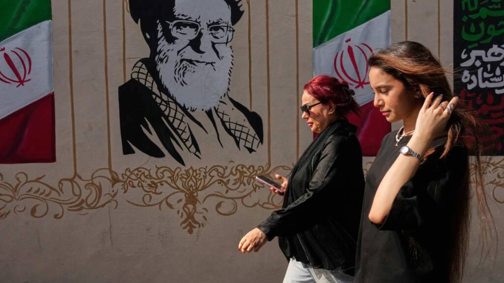ARCHIV - Frauen gehen in der Innenstadt an einem Porträt des verstorbenen iranischen Obersten Führers Ayatollah Ali Chamenei, der bei einem Angriff der USA und Israels am 28. Februar getötet wurde, sowie an Abbildungen der iranischen Flagge vorbei. Foto: Vahid Salemi/AP/dpa/Archivbild