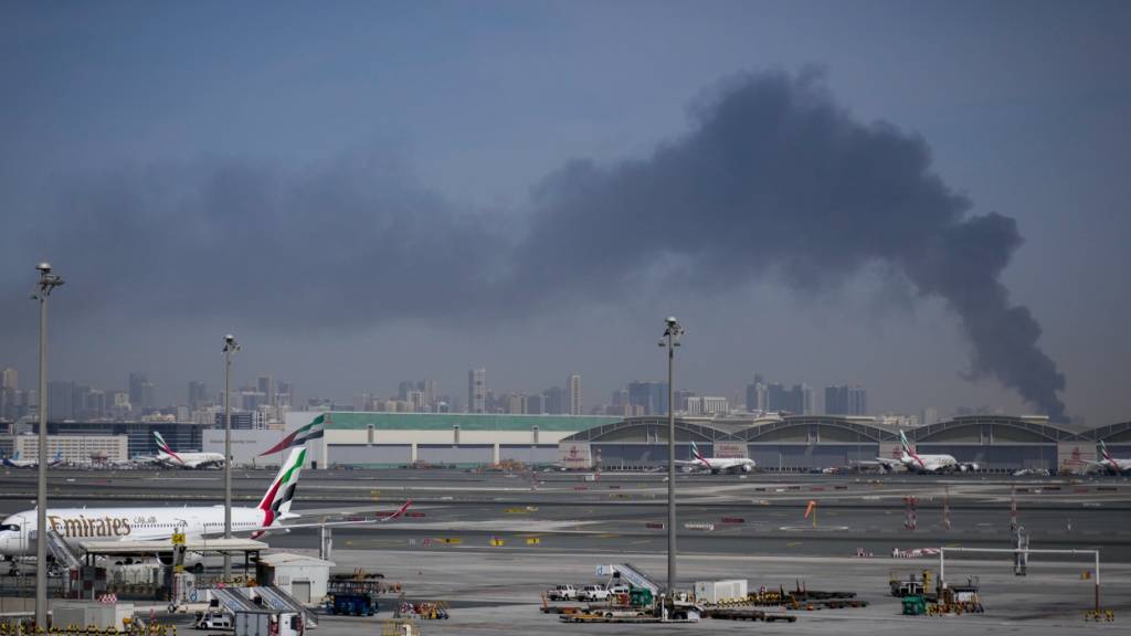 ARCHIV - Eine Rauchwolke, verursacht durch einen iranischen Angriff, ist im Hintergrund zu sehen, während Flugzeuge der Emirates nach der Schließung des Flughafens auf dem Dubai International Airport geparkt sind. Foto: Altaf Qadri/AP/dpa