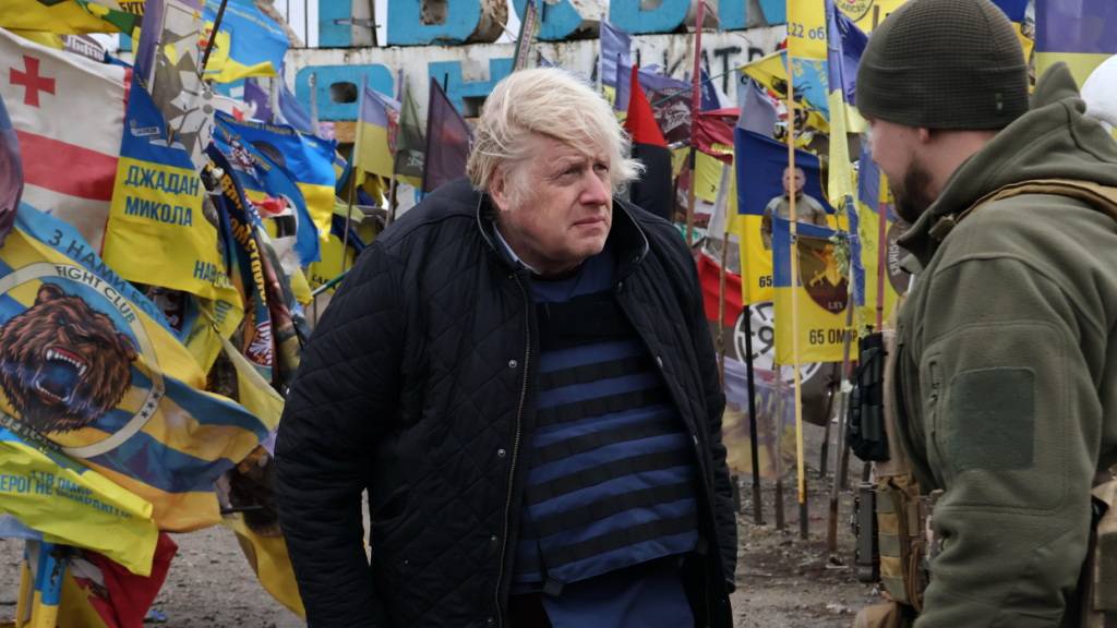 HANDOUT - Auf diesem vom Pressedienst der 65. Mechanisierten Brigade der Ukraine via AP veröffentlichten Foto spricht der ehemalige britische Premierminister Boris Johnson mit einem ukrainischen Soldaten am Ortseingangsschild, umgeben von ukrainischen Nationalflaggen und Flaggen militärischer Einheiten. Foto: Andriy Andriyenko/Ukrainian 65 Mechanized brigade/AP/dpa - ACHTUNG: Nur zur redaktionellen Verwendung im Zusammenhang mit der aktuellen Berichterstattung und nur mit vollständiger Nennung des vorstehenden Credits