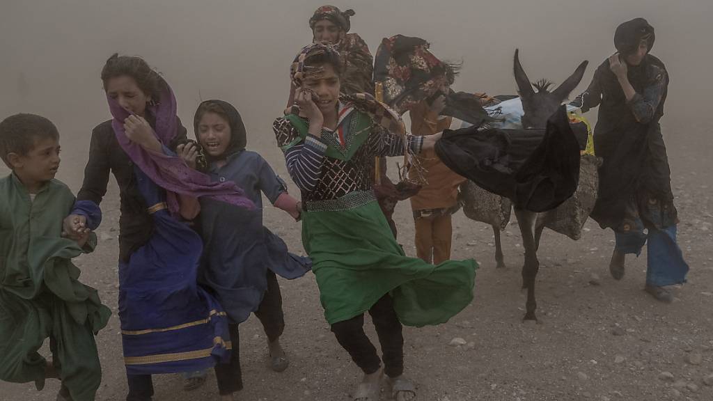 ARCHIV - Afghanische Mädchen und Frauen tragen nach einem Erdbeben im Bezirk Zenda Jan in der Provinz Herat gespendete Hilfsgüter zu ihren Zelten, während eines heftigen Sandsturms. Foto: Ebrahim Noroozi/AP/dpa