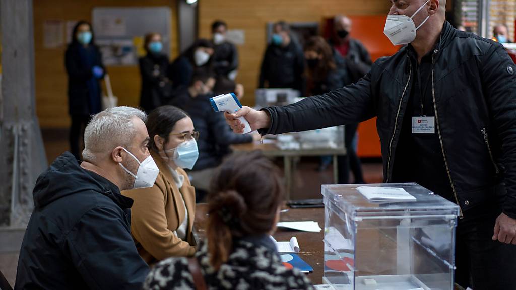 Ein Mann misst die Körpertemperatur der Wahlhelfer in einem Wahllokal während der katalanischen Regionalwahlen. Foto: Emilio Morenatti/AP/dpa
