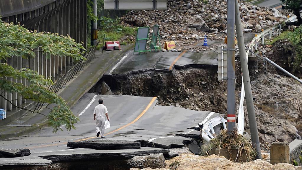 Ein Mann geht auf einer stark beschädigten Straße. Rekordstarke Regenfälle hatten am Wochenende schwere Überflutungen und Erdrutsche im Südwesten Japans ausgelöst.