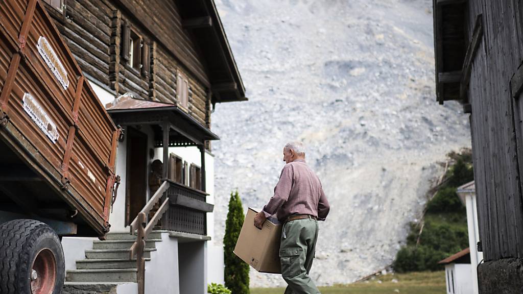 Ein Einwohner von Brienz trägt nach der Aufhebung der Evakuierung Habseligkeiten in sein Haus. Der gewaltige Schuttstrom (im Hintergrund), mit dem sich der Berg entladen hatte, stoppte nur unweit davon.